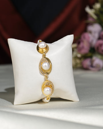 The Trendy White 1 line Bracelet by Chandrani Pearls India features three pearls and sparkling crystals, exuding elegance as it rests on a white cushion with softly blurred flowers in the background.