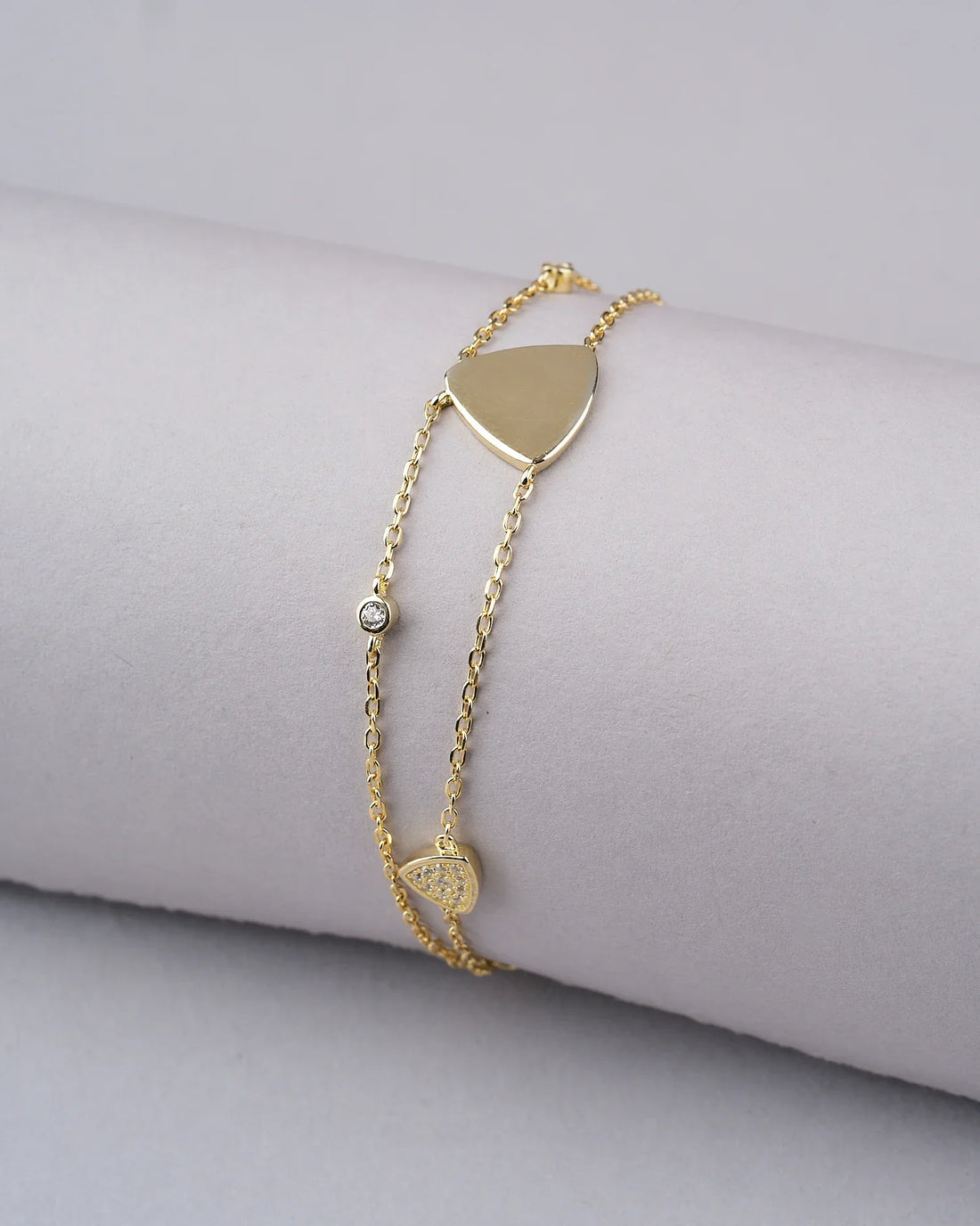 The Triya 925 Silver Gold Bracelet by Chandrani Pearls India, featuring a heart charm and round gem, adds elegance; shown on a ribbed cream surface with red roses in the background.
