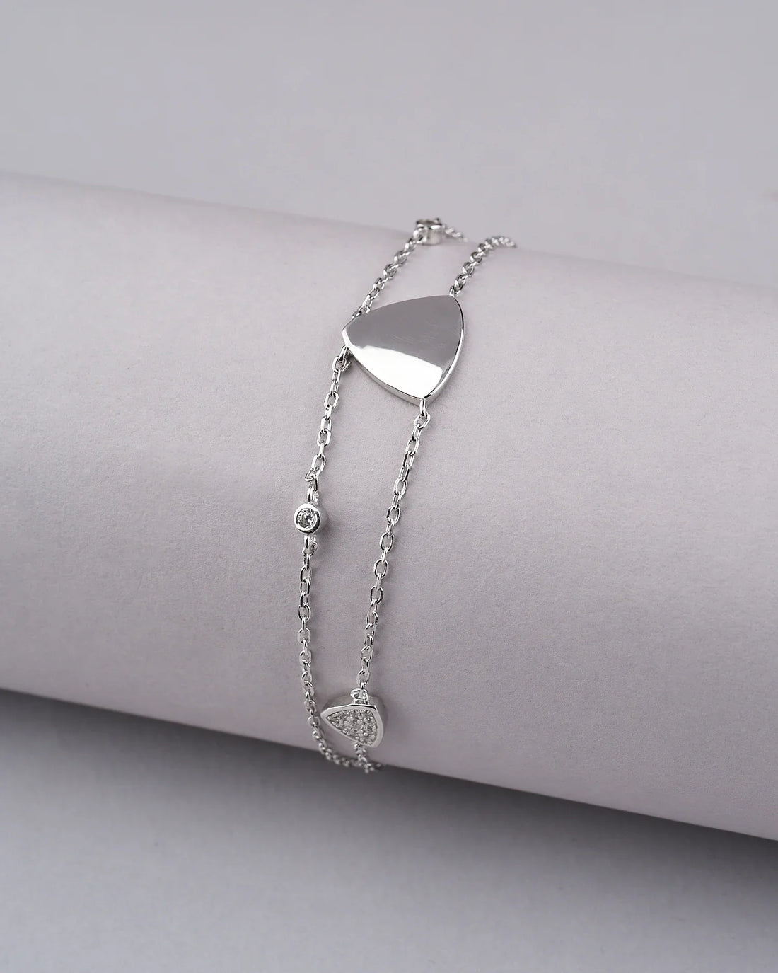 The Tvisha 925 Silver White Bracelet by Chandrani Pearls India features heart and round charms, displayed on a ribbed cylindrical surface with two red roses nearby—perfect for both casual and formal wear.
