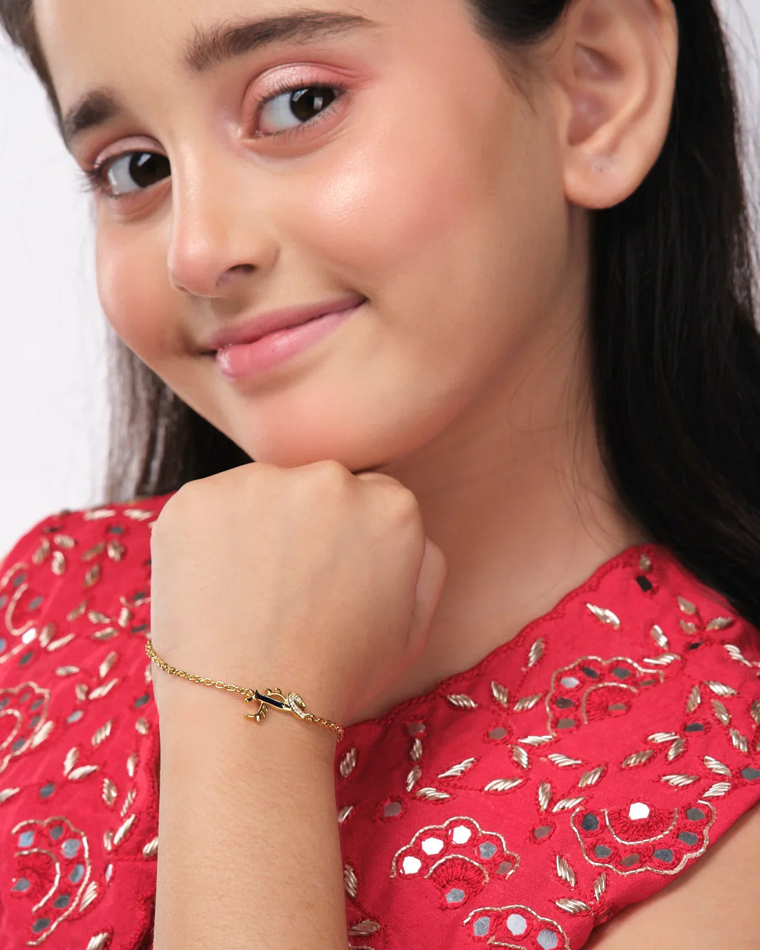 The Dainty Krishna Chain bracelet for kids by Chandrani Pearls India is displayed on a white and navy scalloped backdrop, featuring a blue gem with a leaf design.