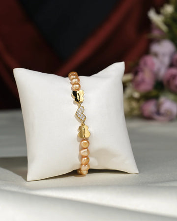 Little Heart CZ Pearl Bracelet by Chandrani Pearls India shown on a white cushion, featuring pearls and a decorative clasp, with blurred flowers in the background.