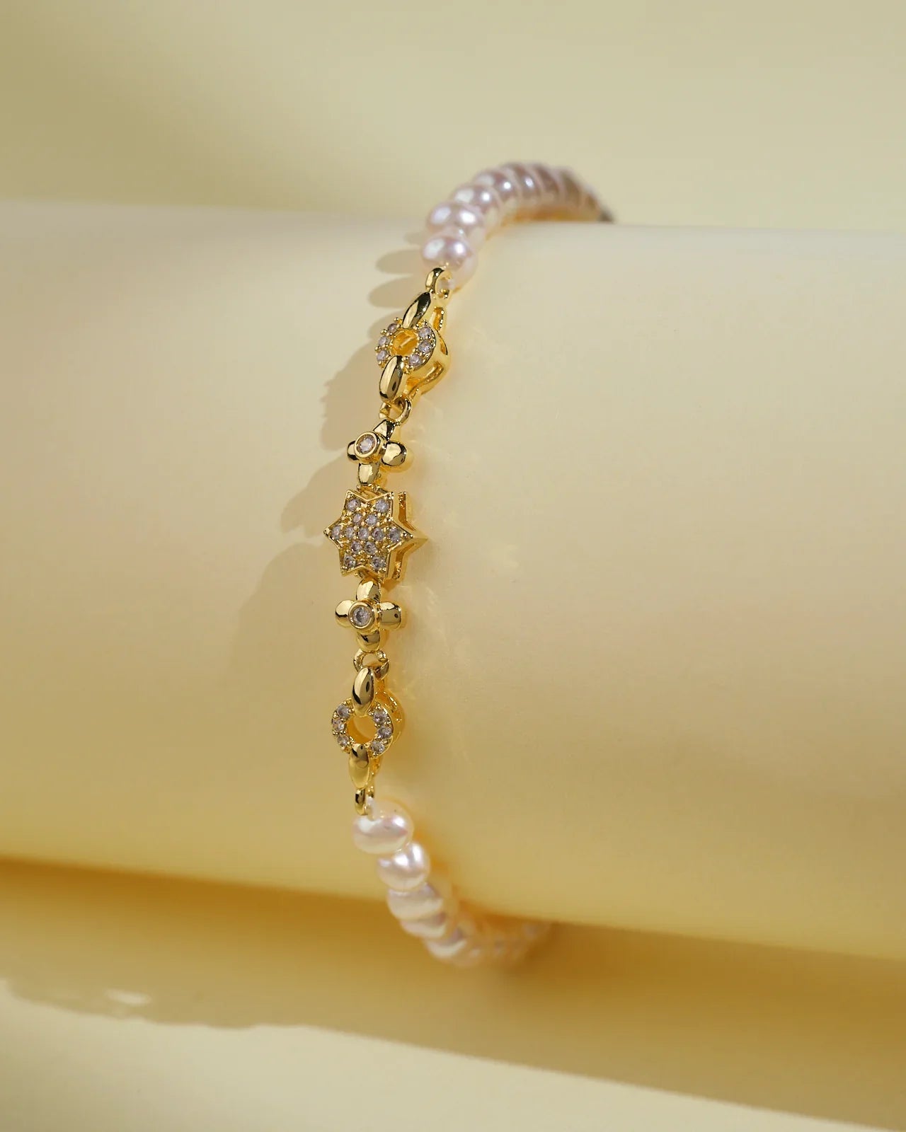 The Flory White 1 Line Pearl Bracelet by Chandrani Pearls India features gold, small floral designs, and clear stones for everyday elegance. Shown against a pale yellow background.