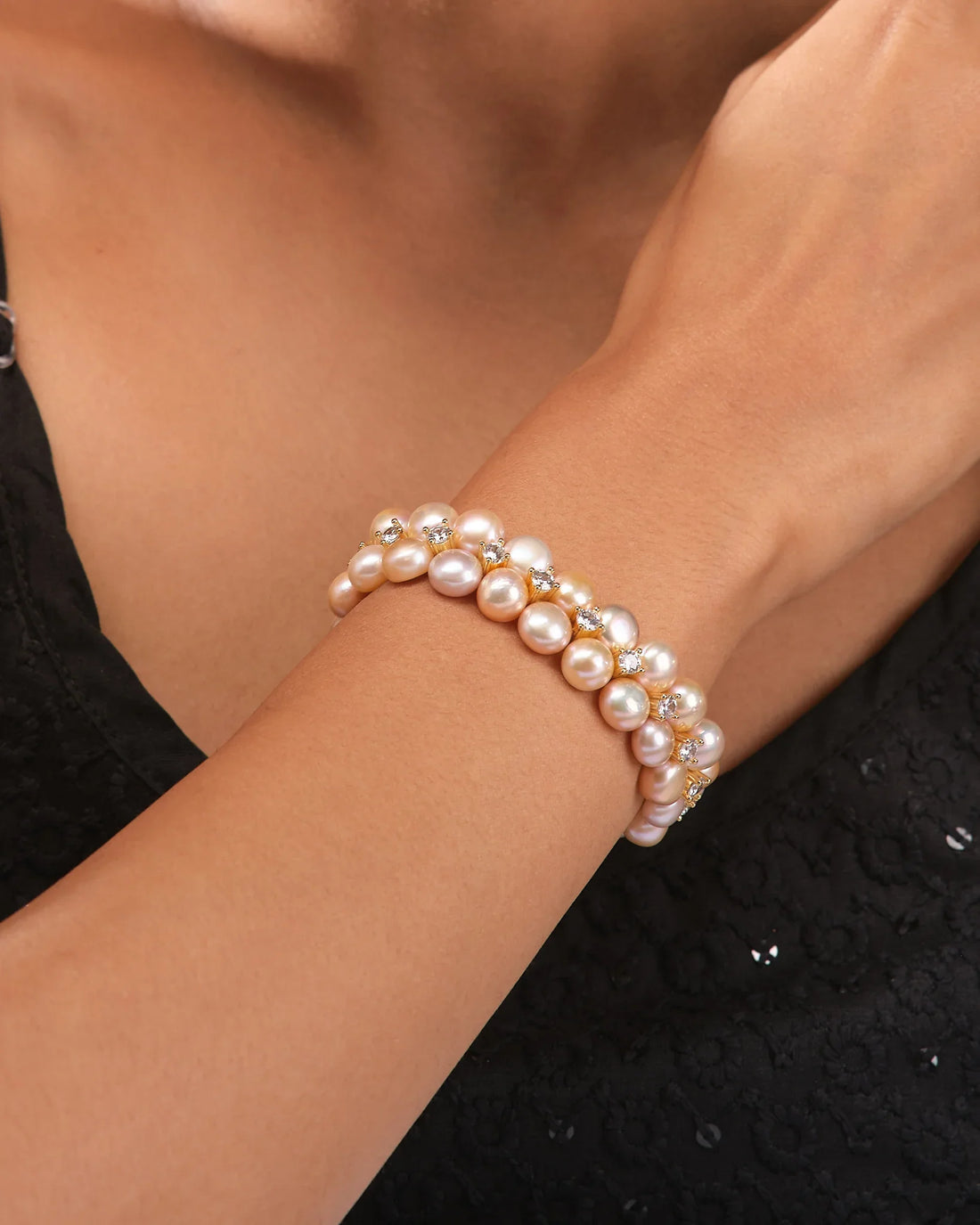 The Lustrous Pearl & Cubic Zirconia Bracelet by Chandrani Pearls is showcased on a dark blue cylinder against a cream fabric backdrop, featuring alternating luminous pearls and sparkling cubic zirconia accents.