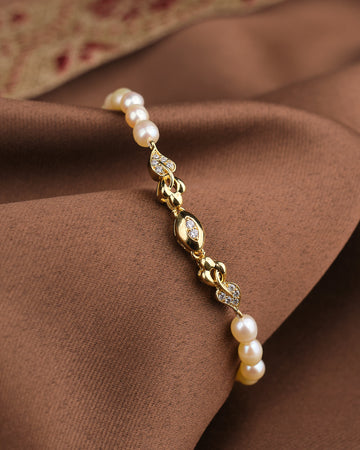 The Noor Pink Light Pearl Bracelet by Chandrani Pearls features blush-toned pearls and CZ stones, displayed on brown fabric—an elegant choice for lovers of feminine jewelry.