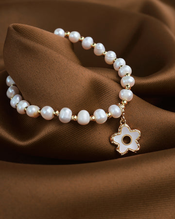 The Soft Radiance bracelet by Chandrani Pearls glows gently with the beauty of mother-of-pearl as it rests on brown fabric, showcasing its elegant charm.