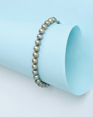 The "Pearls that speak elegance" bracelet by Chandrani Pearls, featuring round metallic-hued pearls, is displayed on light blue paper and adds chic sophistication to any look.