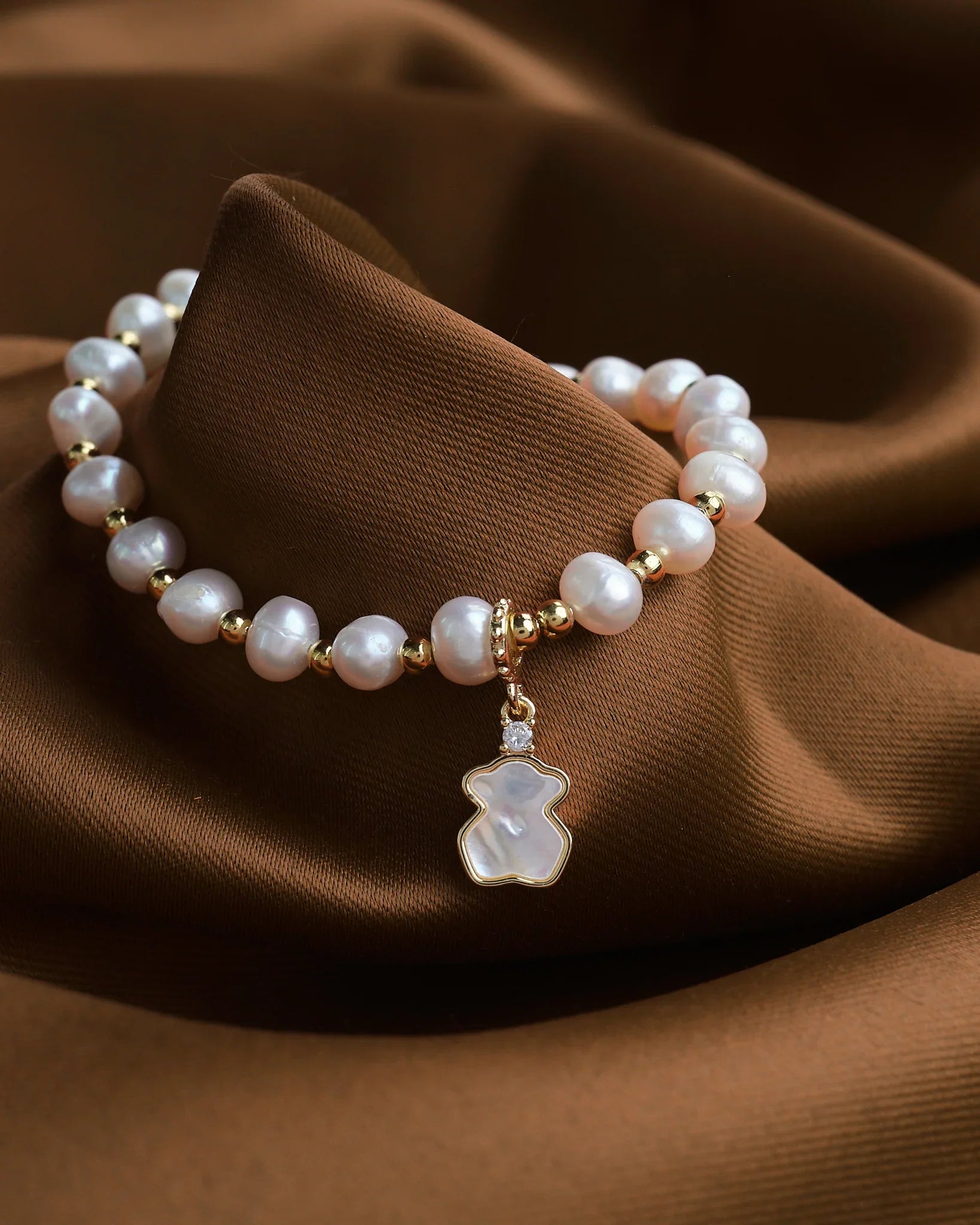 Refined Layers by Chandrani Pearls: This stackable bracelet features lustrous pearls, gold accents, and a teddy bear-shaped charm, creating a charming sea-inspired accessory for any ocean jewelry collection.