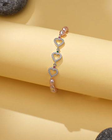 The Chandrani Pearls Dainty Heart Shaped Pearl Bracelet with CZ Halo Accents is displayed on a light yellow surface with gray stones nearby.