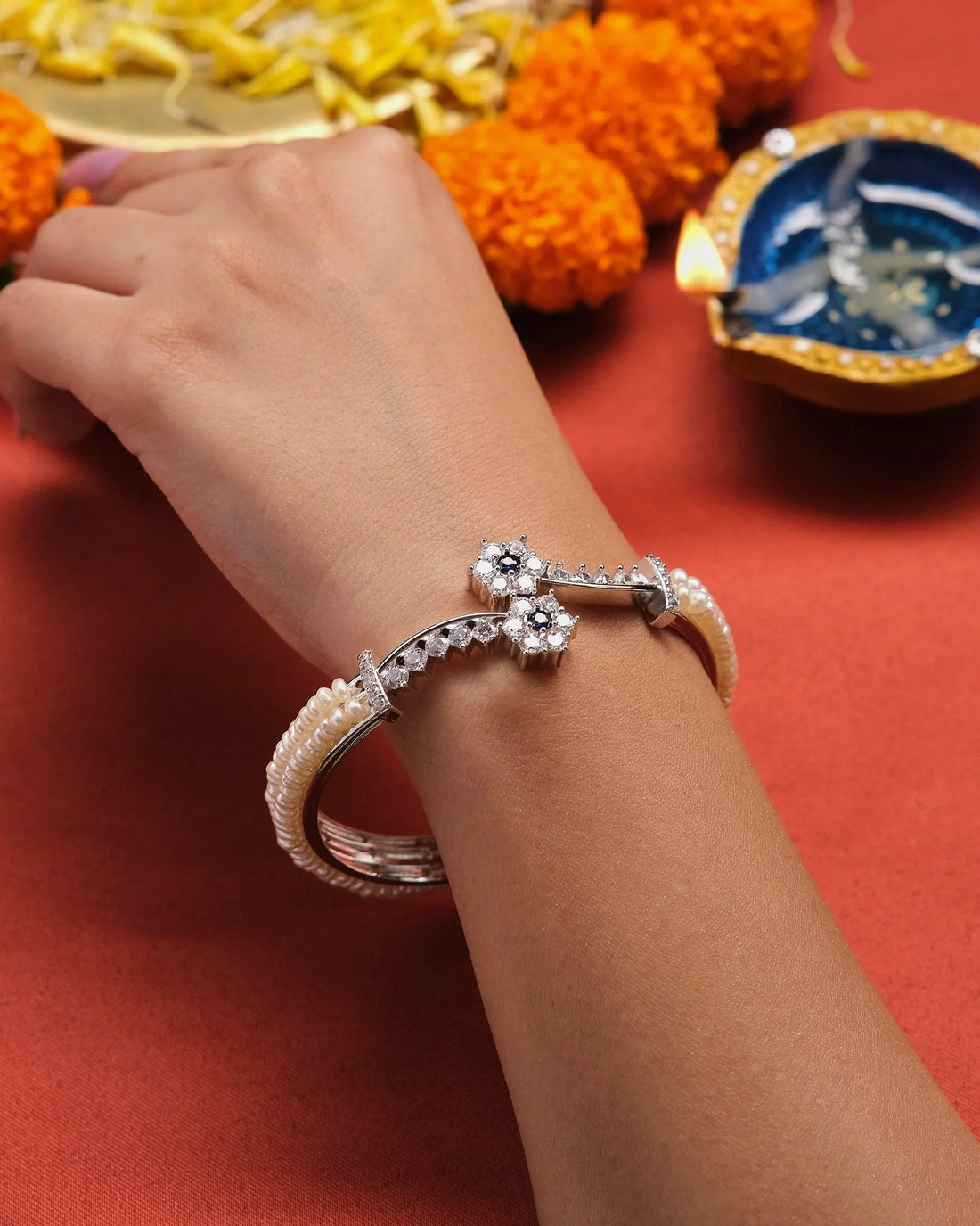 The Buzzing Sweetness Pearl Bangle from Chandrani Pearls, embellished with pearls and star-shaped accents, is elegantly displayed on a red box against a bokeh background.
