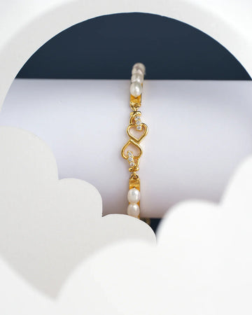 The Posy Heart Pearl Bangle for kids by Chandrani Pearls India is elegantly displayed on a white stand, accompanied by cloud-shaped cutouts.