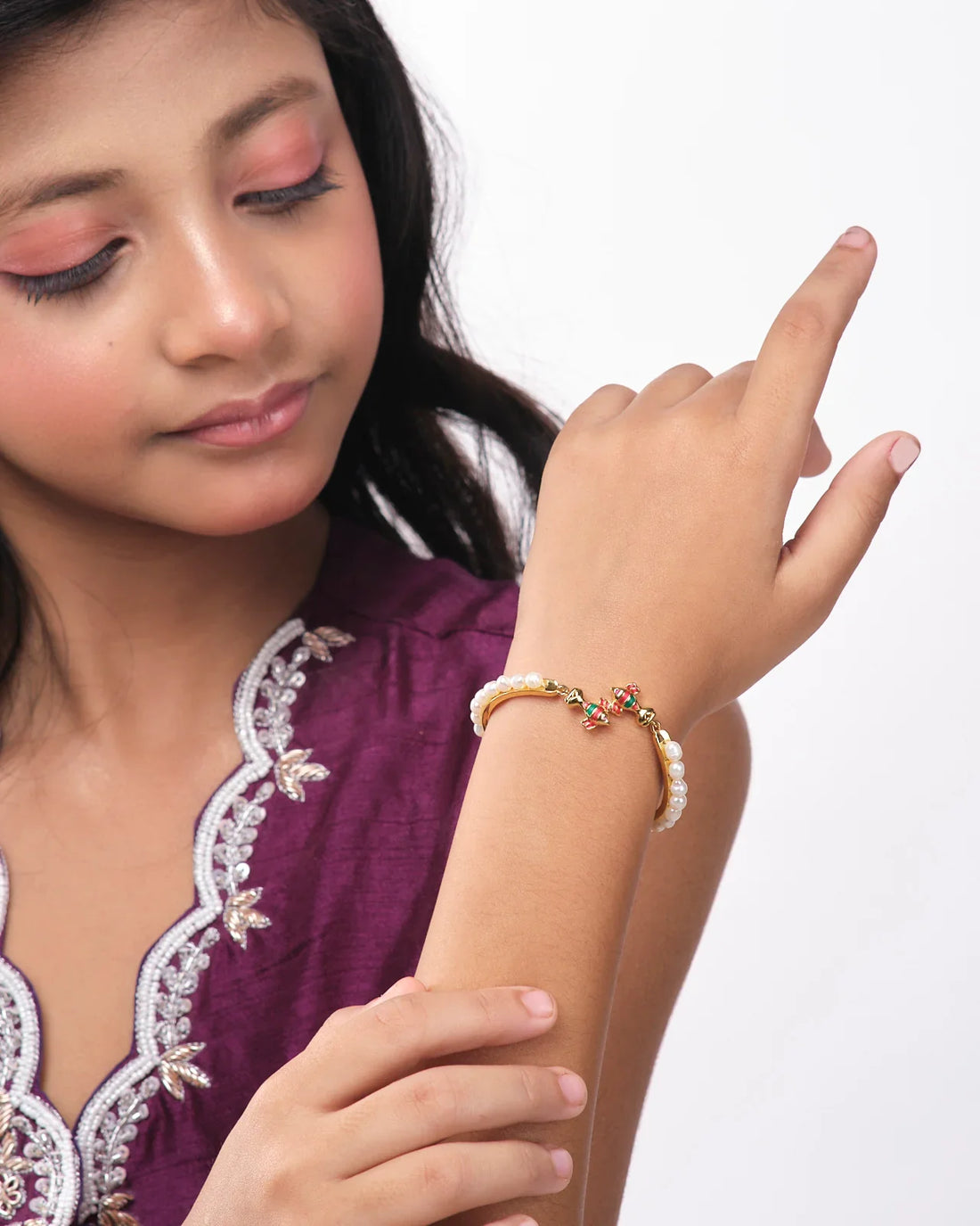 The Fishy Pearl Bangle for kids by Chandrani Pearls India, featuring gold with pearl accents and colorful bird ornaments, is displayed on a white and blue backdrop.