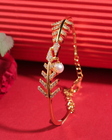 The Ara and Pearl 925 Silver Bangle by Chandrani Pearls India features a leaf motif with crystal accents and a pearl charm, shown on a red surface against a red and pink floral background.