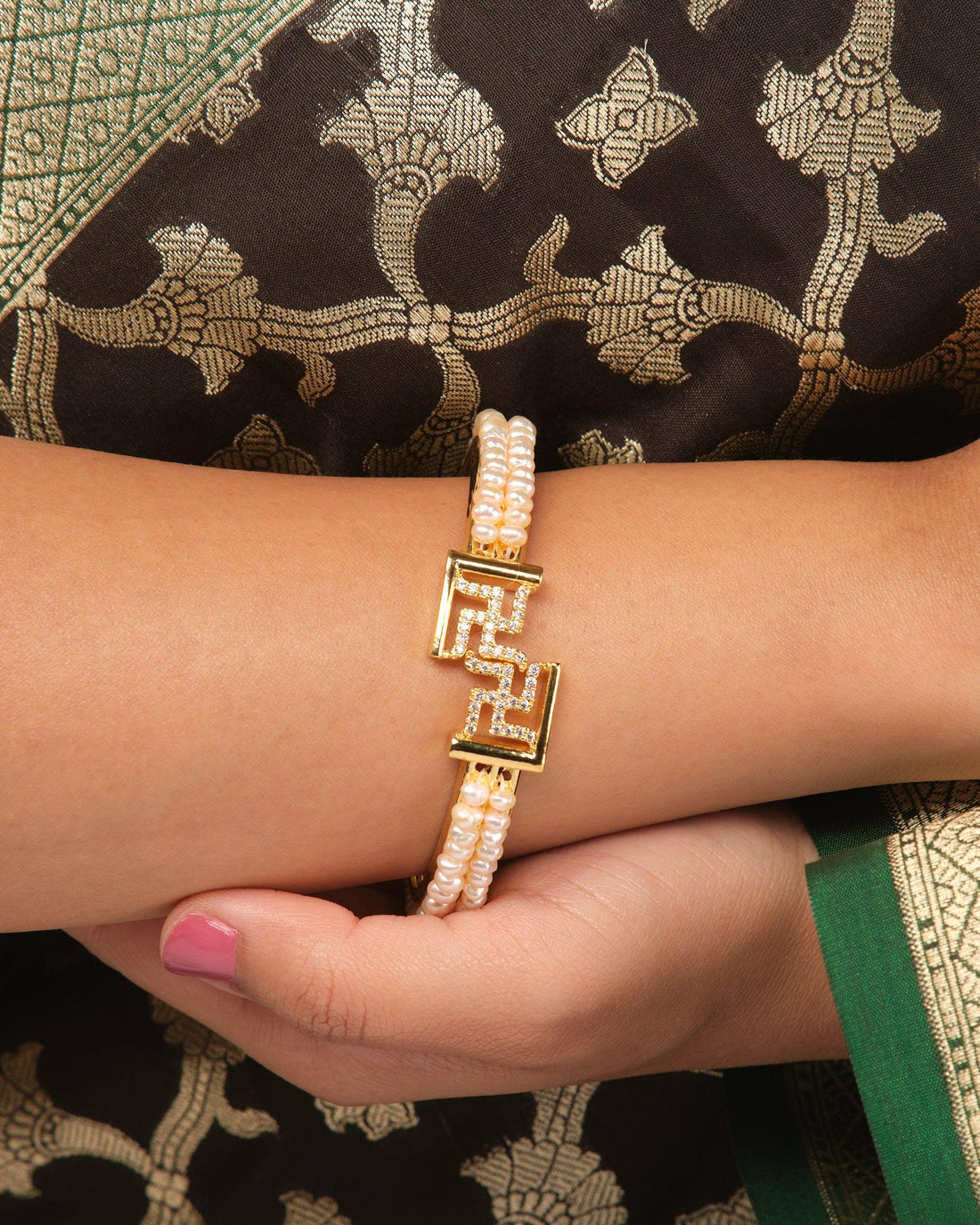 Swasthik White Pearl & CZ Cuff Bangle by Chandrani Pearls—a chic statement piece with two rows of small pearls, CZ stones, and a geometric clasp, styled on a light beige surface with smooth gray stones in the background.