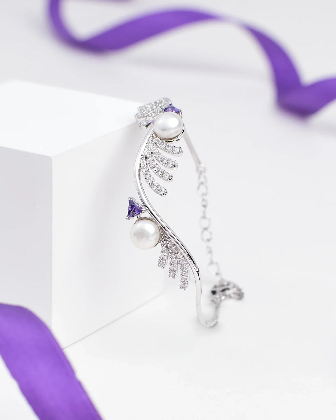 The Chandrani Pearls Luxury Tennis Bracelet in Sterling Silver with CZ Stones is showcased on a white block, accented by a purple ribbon in the background.