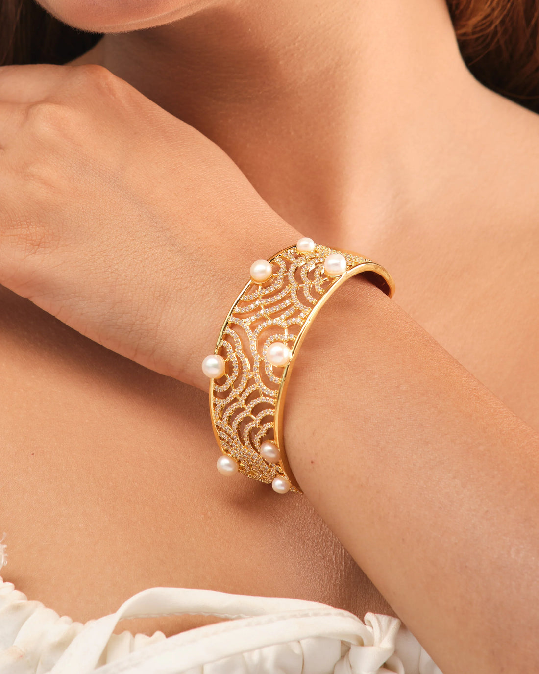 The Stunning pearl bangle accented with sparkling CZ stones by Chandrani Pearls is displayed on a round white platform against a blue background.