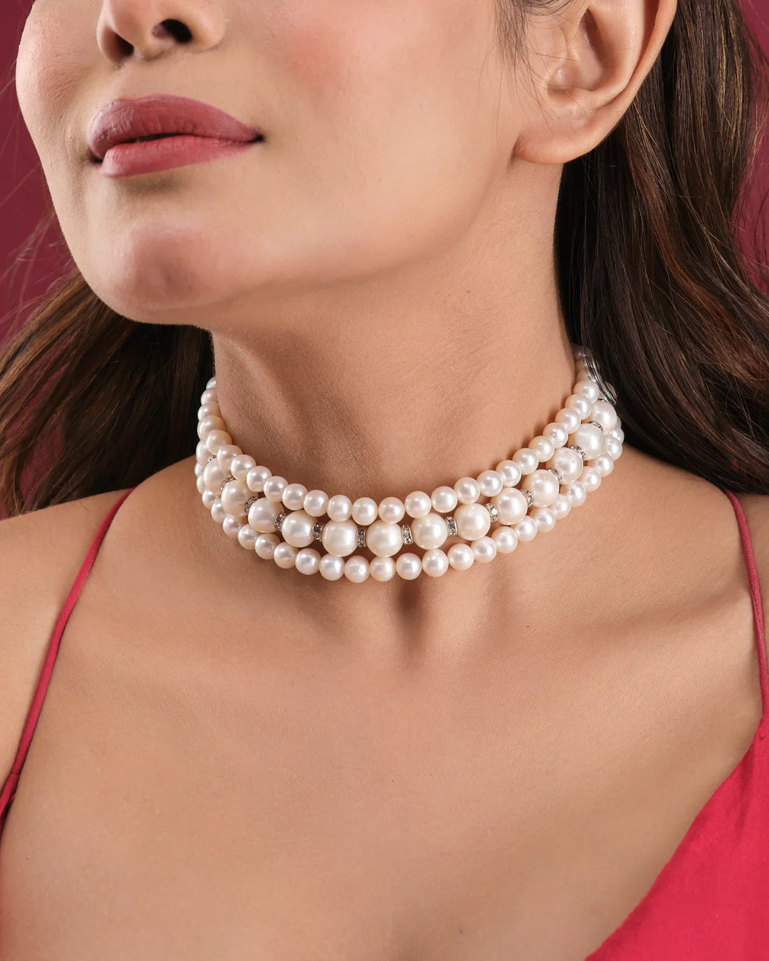 The Elegant Triple Line Choker by Chandrani Pearls India showcases refined glamour on a white jewelry stand, set against a softly blurred floral backdrop.