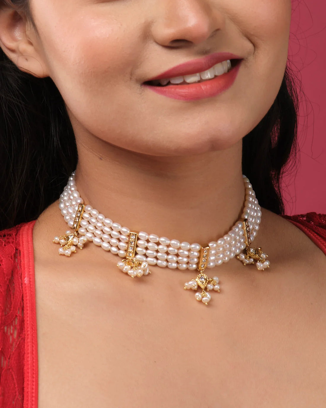 The Gorgeous 4 Line Pearl Choker by Chandrani Pearls India features gold and pearl floral pendants, exuding natural elegance on a white jewelry stand set against a dark background with purple flowers.