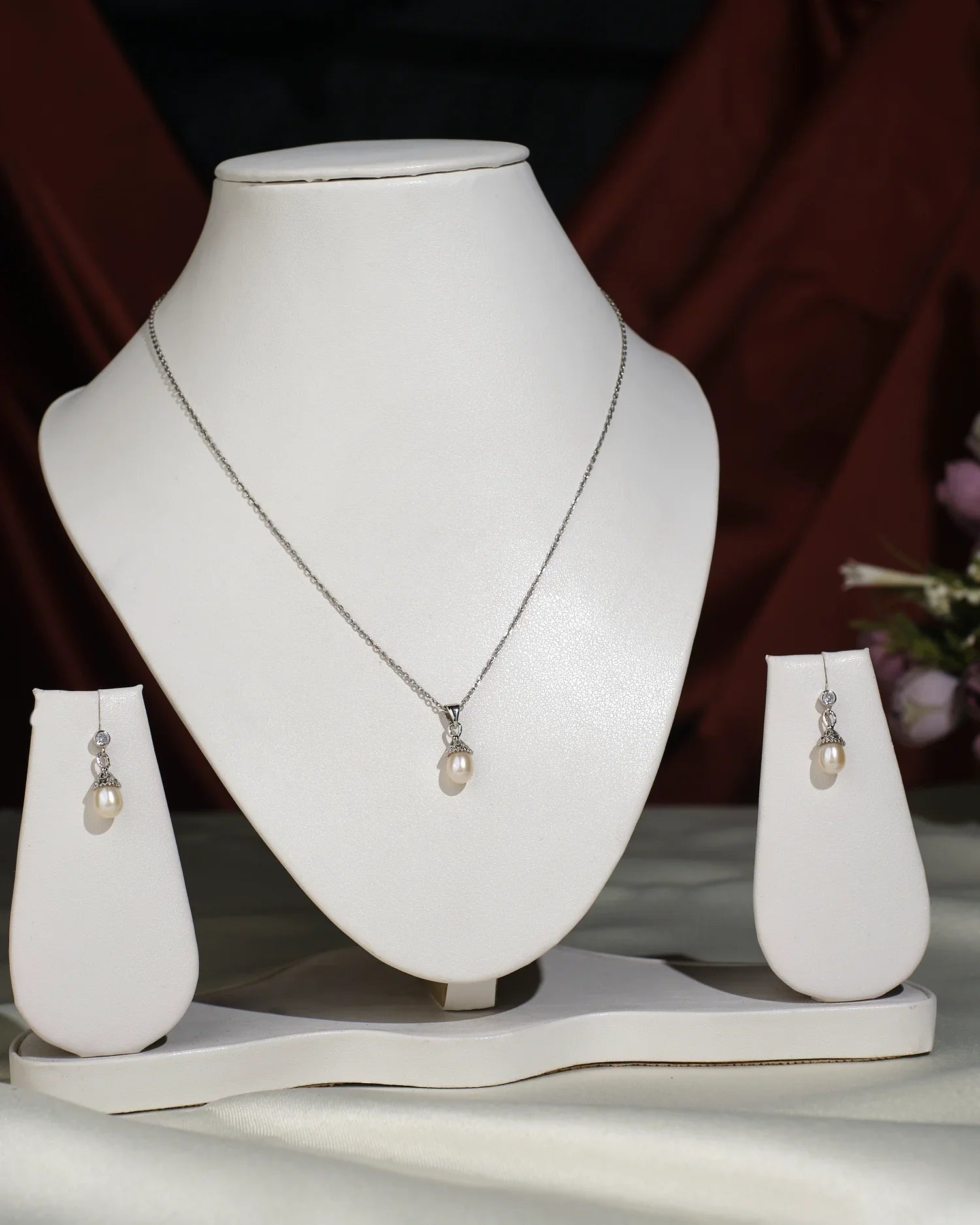 The Pretty Pendant Set by Chandrani Pearls India includes a single pearl pendant and matching pearl drop earrings, displayed on a white jewelry stand for an elegant look. (Chain shown is for photographic purpose only.).