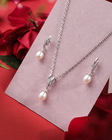 The Riley 925 Silver White Pendant Set by Chandrani Pearls India features a classic design with matching earrings and pearl drops, displayed on a pink card with red roses—ideal for any occasion.