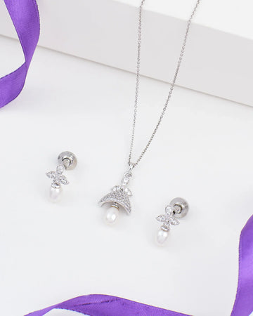 The Luna Drop Pendant Set by Chandrani Pearls features a 925 sterling silver necklace and matching earrings with pearls and CZ accents, displayed on a white surface with purple ribbon accents.