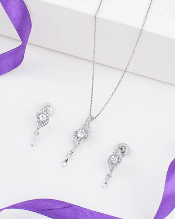 The Chandrani Pearls Floral Grace Pendant Set in sterling silver with CZ and pearl is displayed on a white surface next to a purple ribbon.
