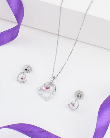 The Chandrani Pearls Heart Pendant Set in sterling silver features a heart-shaped necklace and matching earrings with CZ stones, beautifully displayed on a white surface with purple ribbon accents.