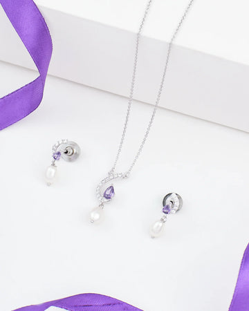 The Modern Chic Pendant Set by Chandrani Pearls features 925 silver necklace and earrings with purple CZ gemstones and pearl drops, elegantly displayed on a white surface with purple ribbon accents.