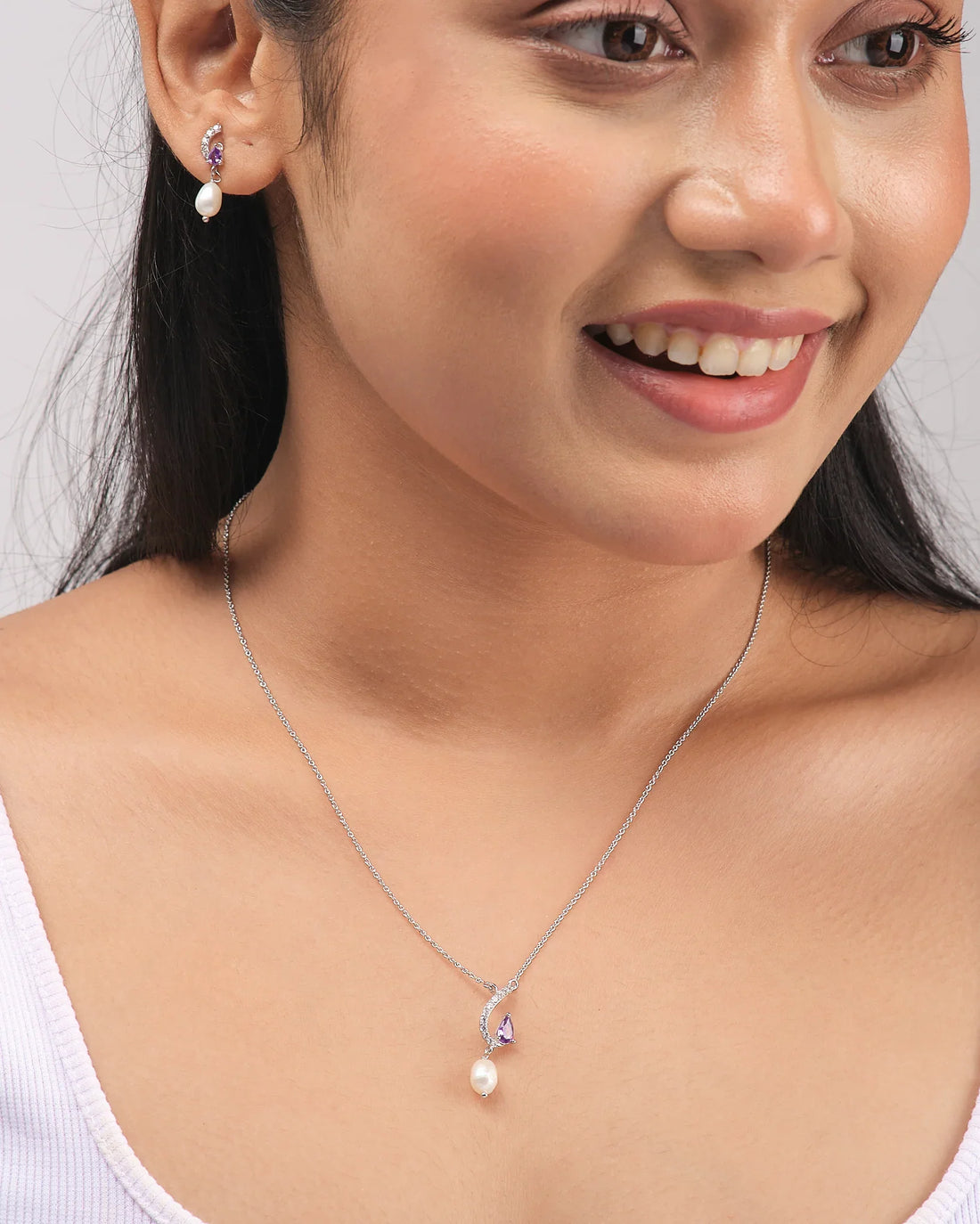 The Modern Chic Pendant Set by Chandrani Pearls features 925 silver necklace and earrings with purple CZ gemstones and pearl drops, elegantly displayed on a white surface with purple ribbon accents.