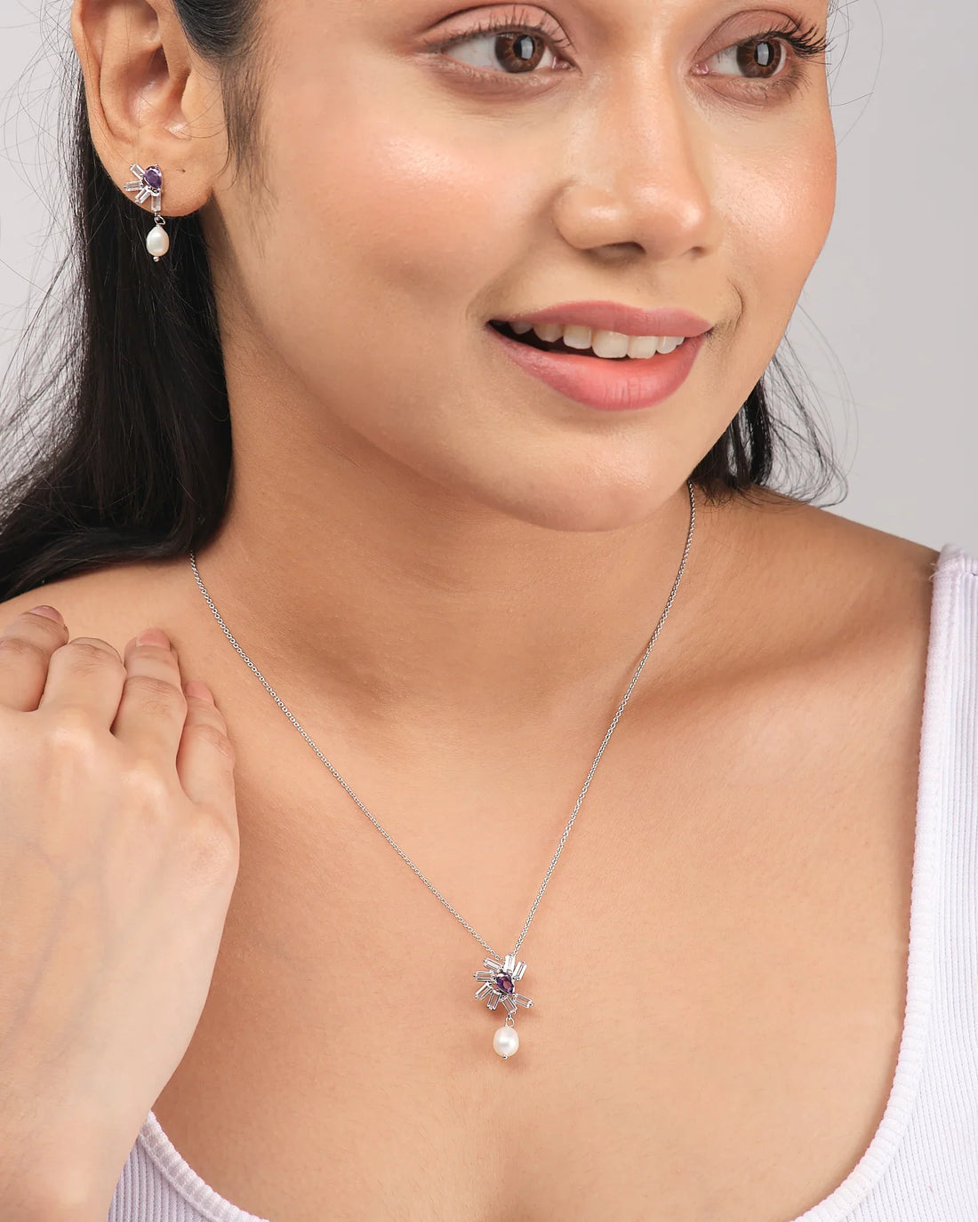 The Chandrani Pearls Twilight Teardrop Pendant Set features a sterling silver necklace and matching earrings with purple gemstones, CZ accents, and white pearls, displayed on a white surface with purple ribbon accents.