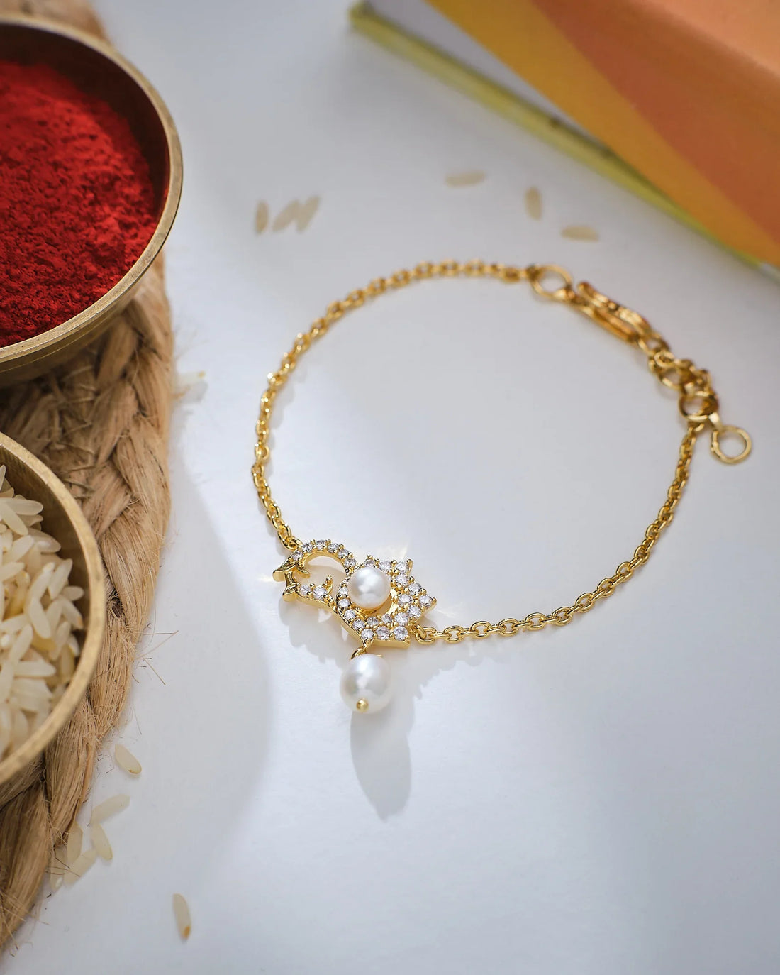 A person wearing the Go With The Flow Pearl Bracelet by Chandrani Pearls, paired with a yellow outfit, adjusts the accessory on their wrist. A decorated plate in the background enhances the timeless elegance of this look.