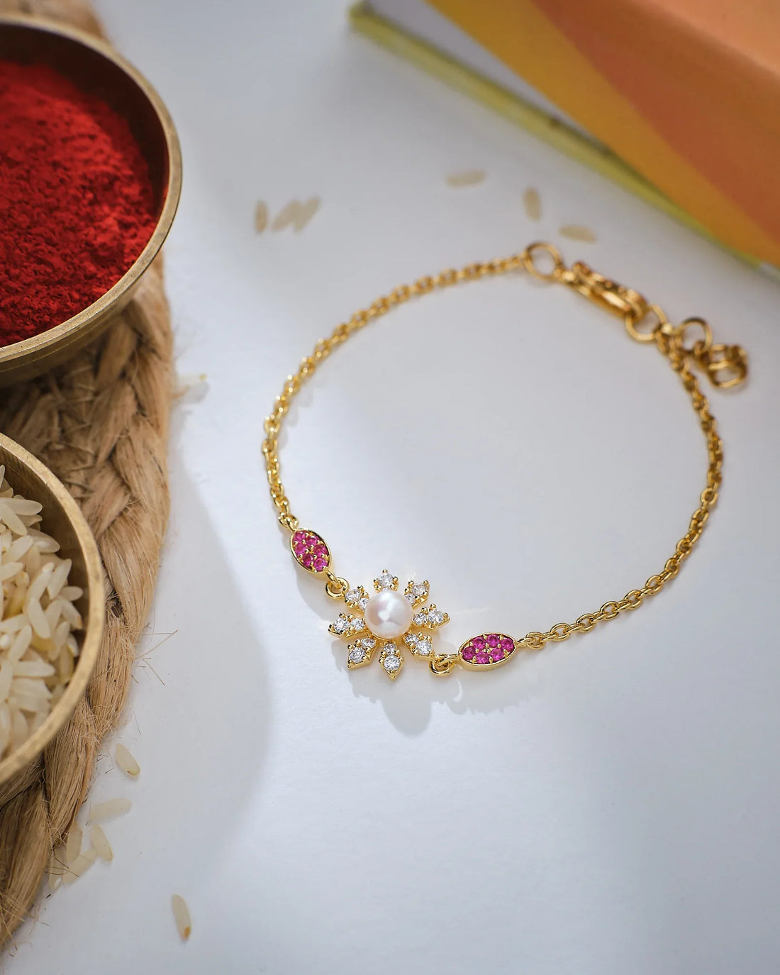 A hand wears the Adorable Flower Pearl Bracelet by Chandrani Pearls, adorned with pearls, clear stones, and pink gems in a floral motif, as another person helps fasten it.