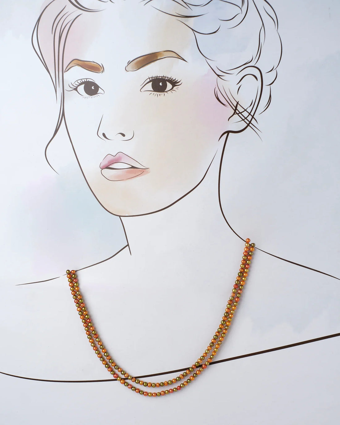 The Hiranya Multi Colour Pearl Necklace by Chandrani Pearls features two lustrous metallic bead strands in gold and copper hues, set against a purple and lavender backdrop with blurred floral details.