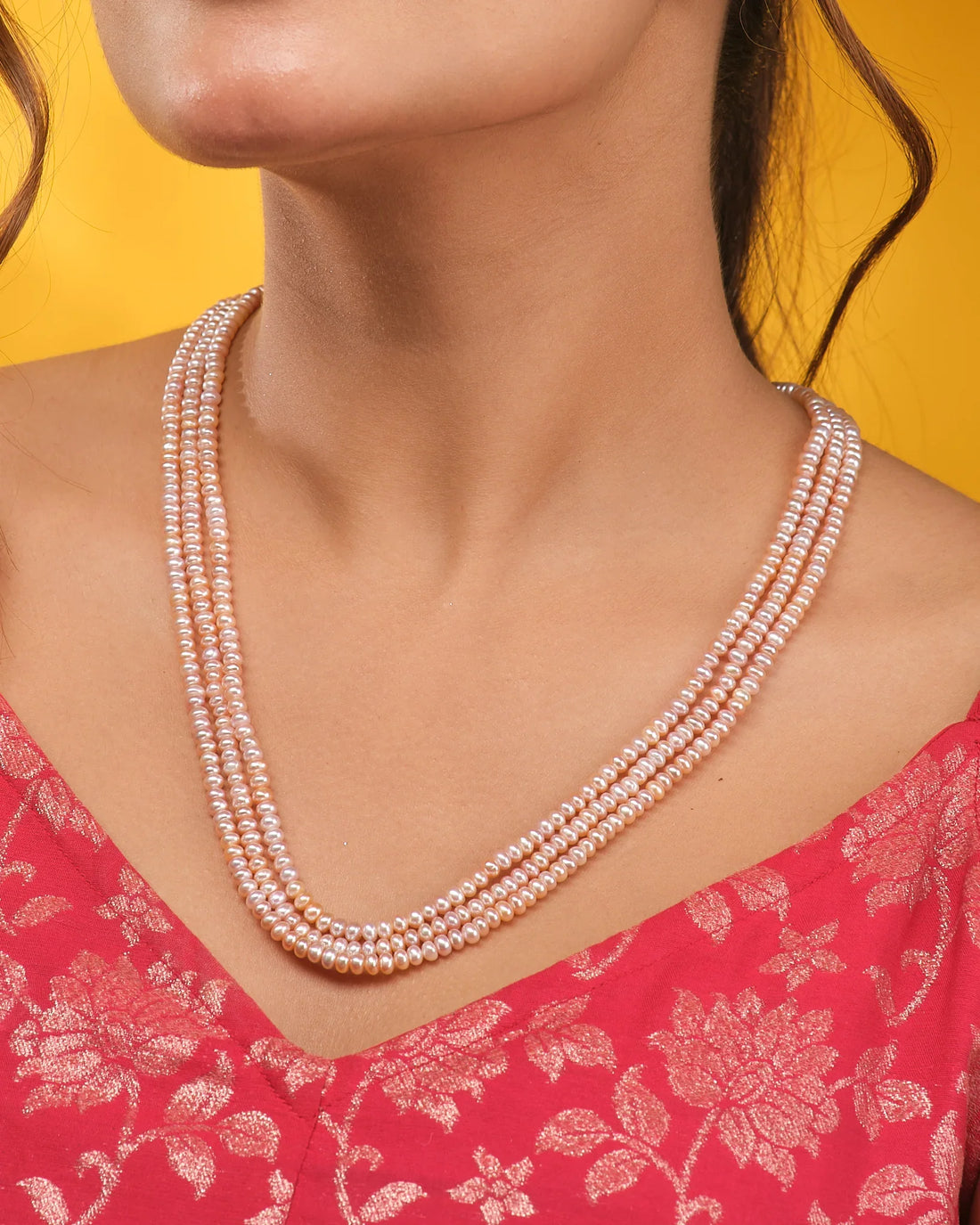 The Chandrani Pearls Freshwater Pink Pearl Necklace, featuring three lustrous strands, is elegantly displayed on a black velvet bust with cream satin fabric accents.