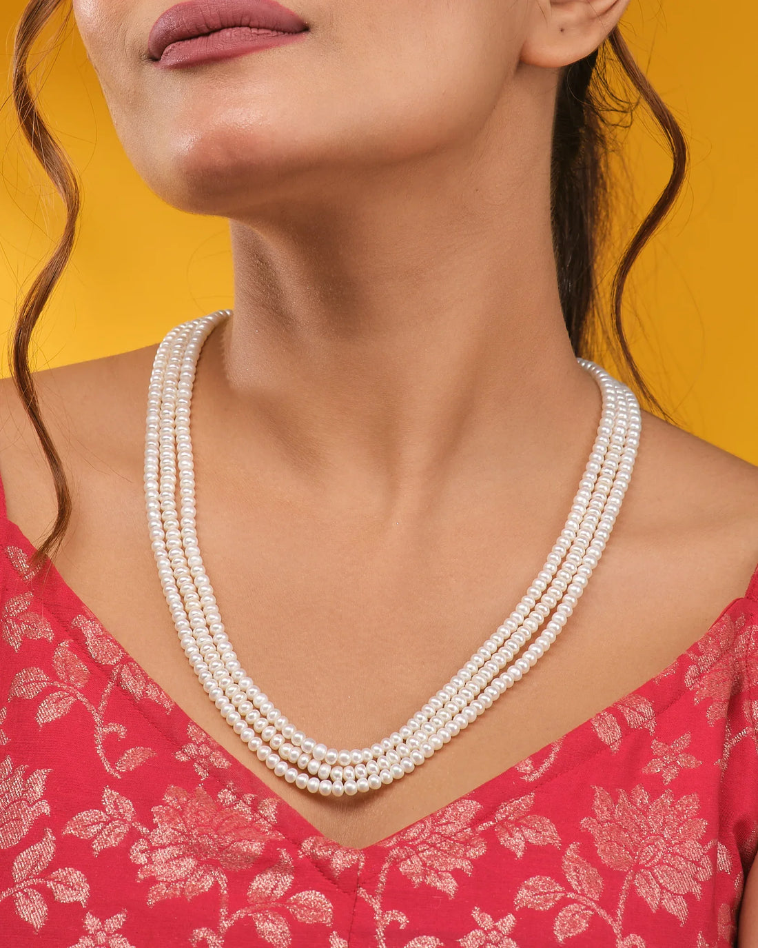 A sophisticated display showcases the Chandrani Pearls Classic White Pearl Necklace on a dark blue velvet bust, set against cream fabric in the background.