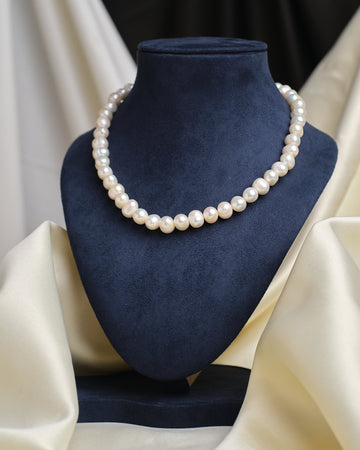 The Classic Elegance Pearl Necklace by Chandrani Pearls is showcased on a blue velvet bust with cream draped fabric, highlighting its timeless beauty—an exquisite pearl jewelry piece for any occasion.
