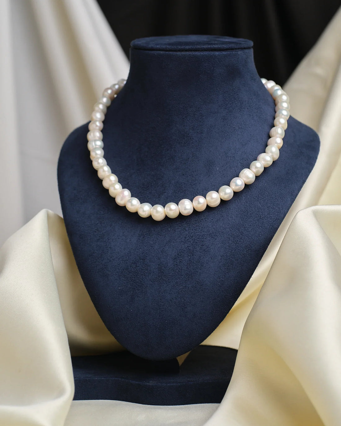 The Classic Elegance Pearl Necklace by Chandrani Pearls is showcased on a blue velvet bust with cream draped fabric, highlighting its timeless beauty—an exquisite pearl jewelry piece for any occasion.