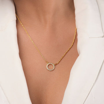 The Circle of Life Pendant by Chandrani Pearls is a gold-plated chain necklace featuring a circular pendant adorned with sparkling cubic zirconia, styled here with a white collared top.