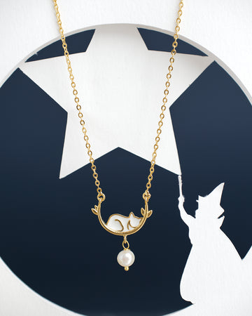 The Sleepy Cat Pretty Pendant by Chandrani Pearls India, featuring a gold finish with a fox and pearl design, is showcased against a backdrop highlighting a wizard's silhouette and star.