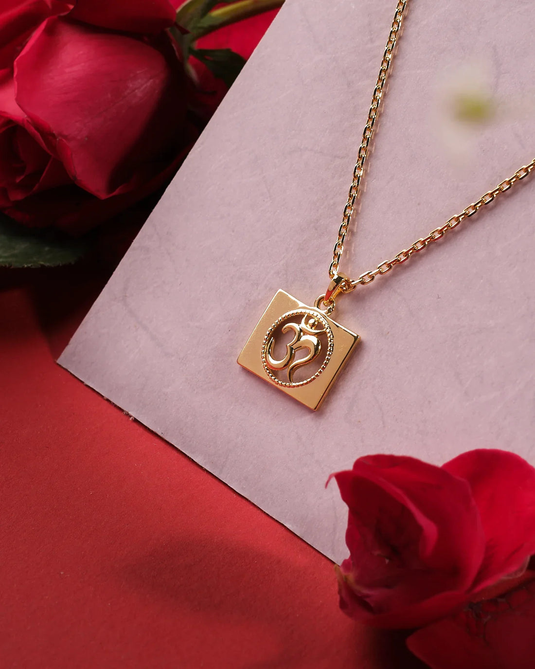 The Omkara 925 Silver Pendant by Chandrani Pearls India features an Om symbol on a square charm, elegantly displayed on a light pink surface with red roses for a refined touch.