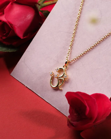 The OM 925 Silver Pendant by Chandrani Pearls India, featuring a chic "Om" design with clear stones, displayed on a pink surface near red roses, is a stylish accessory that elevates your look.