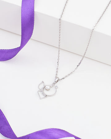 The Demifine Radiance Pendant by Chandrani Pearls features a delicate 925 silver design with CZ and pearl, beautifully displayed on a white surface with a purple ribbon.