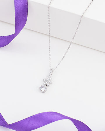 The Chandrani Pearls Minimalist Demifine Silver Pendant with Solitaire CZ features a sparkling solitaire stone in a sleek silver setting, shown on a white surface with a touch of purple satin ribbon for added elegance.