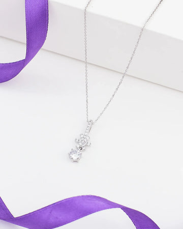 The Chandrani Pearls Minimalist Demifine Silver Pendant with Solitaire CZ features a sparkling solitaire stone in a sleek silver setting, shown on a white surface with a touch of purple satin ribbon for added elegance.