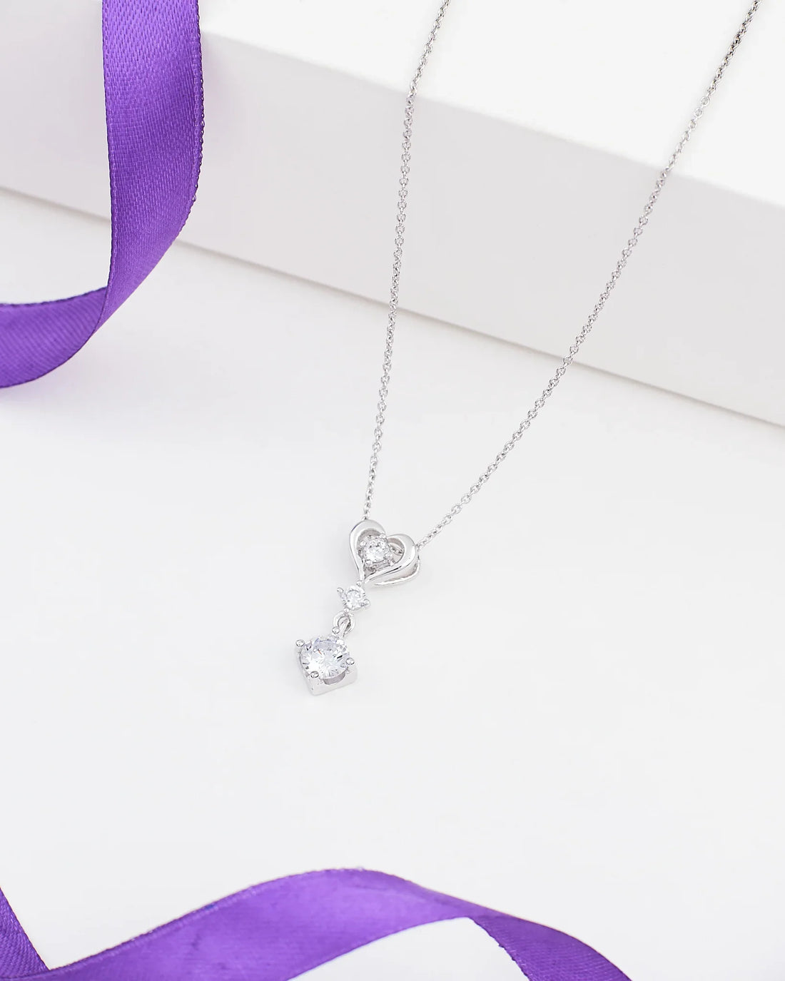 The Pendant with Little Heart of CZ in Demifine Silver by Chandrani Pearls, displayed on a white surface with a purple ribbon, adds sophisticated shine to any look with its heart design and sparkling CZ stone drop.