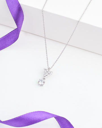 The Floral CZ Pendant in Elegant Demifine Silver by Chandrani Pearls features a butterfly-shaped design with a single round CZ stone, shown on a white surface and accented with a purple ribbon.