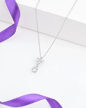 The Floral CZ Pendant in Elegant Demifine Silver by Chandrani Pearls features a butterfly-shaped design with a single round CZ stone, shown on a white surface and accented with a purple ribbon.