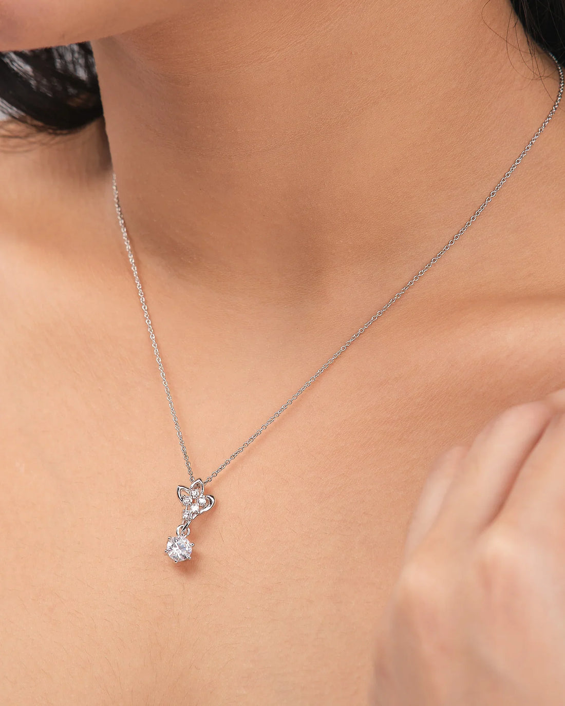The Floral CZ Pendant in Elegant Demifine Silver by Chandrani Pearls features a butterfly-shaped design with a single round CZ stone, shown on a white surface and accented with a purple ribbon.