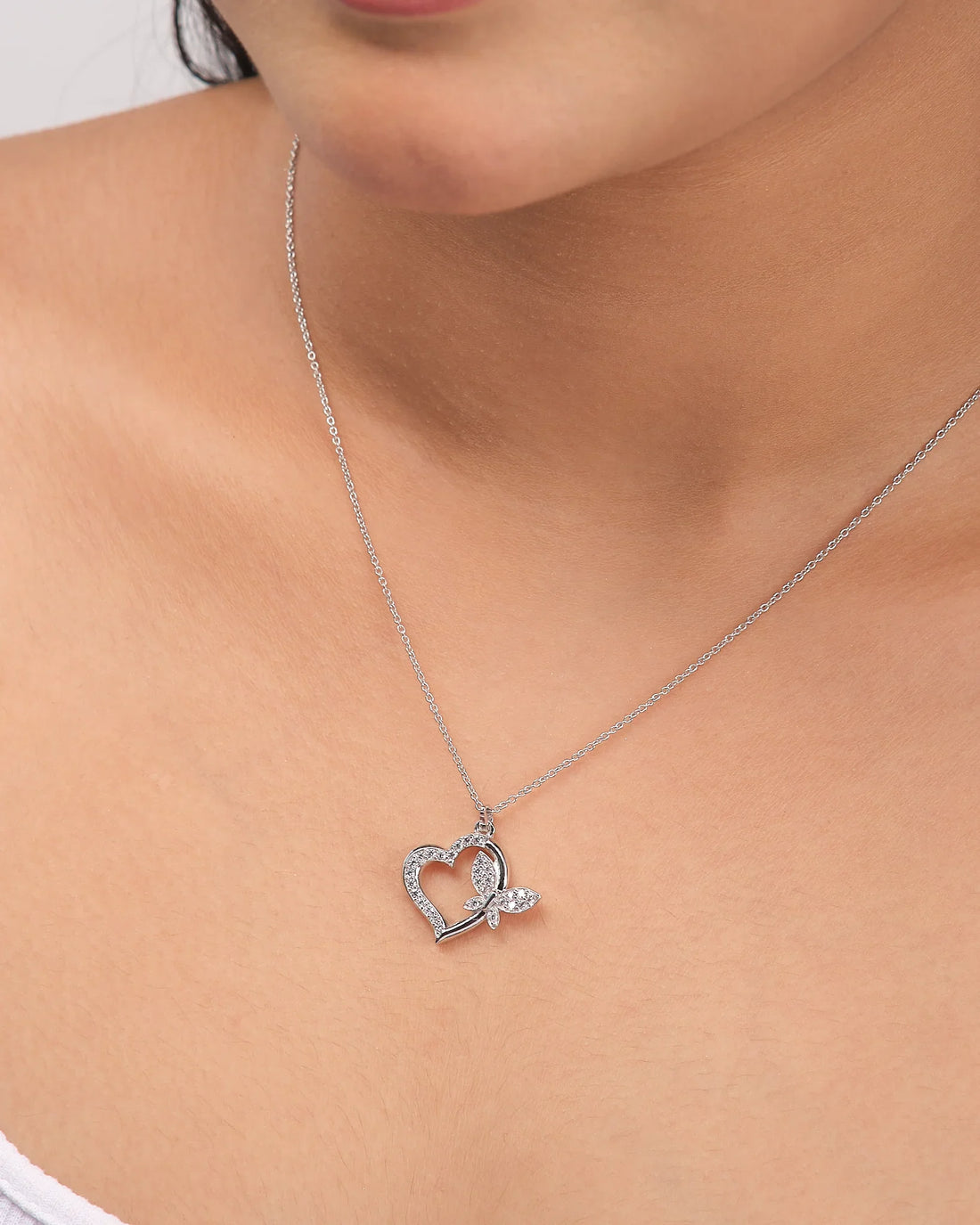 The Chandrani Pearls Heart-Butterfly Demifine Silver CZ Pendant features a heart-butterfly shape with sparkling crystals and leaf detail, shown on a white surface with a purple ribbon.