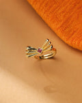 The Trendy Beautiful Ring by Chandrani Pearls, featuring a gold polish, fan-shaped bow design, and central square CZ stone, is displayed on a beige surface beside orange textured fabric.