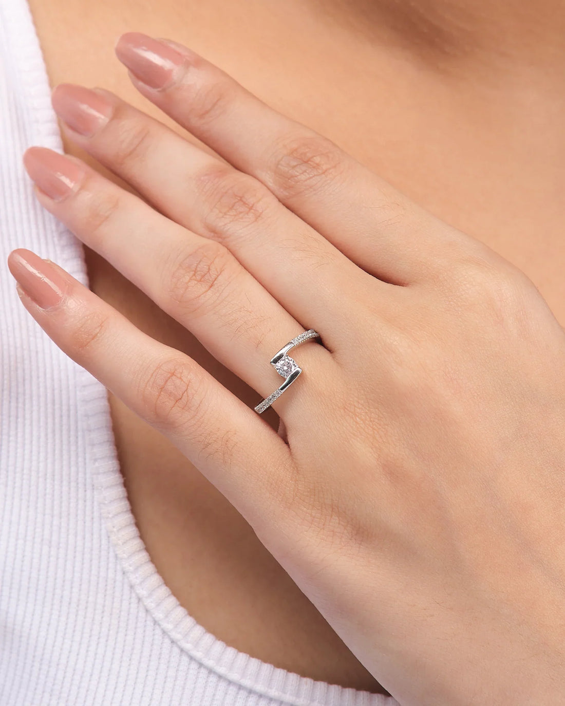 The Solitaire CZ Promise Ring in Demifine Silver by Chandrani Pearls features a round central CZ stone and small side stones, shown on a white surface with a purple ribbon in the background.
